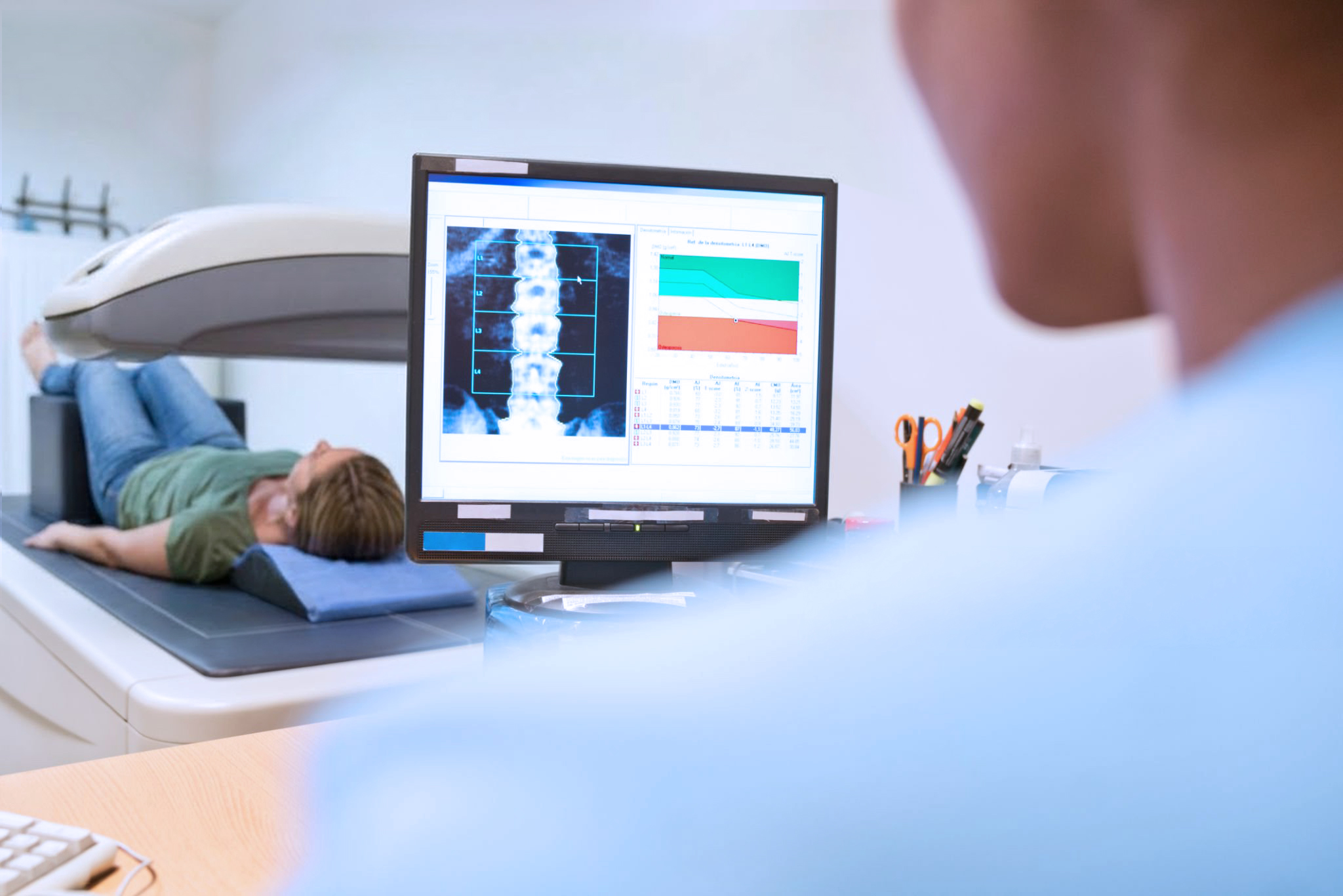 Midsection of female healthcare worker analyzing x-ray image on computer monitor. Senior male patient is lying on examination table. They are in hospital ward.